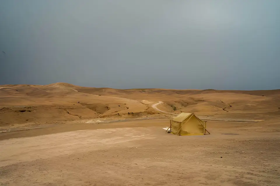 A single tent on a wide, bare desert plain under a grey sky