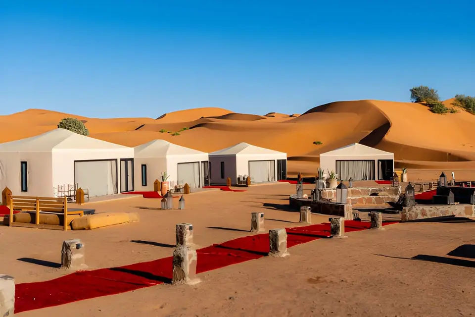 A row of white tents in a camp at the foot of orange sand dunes