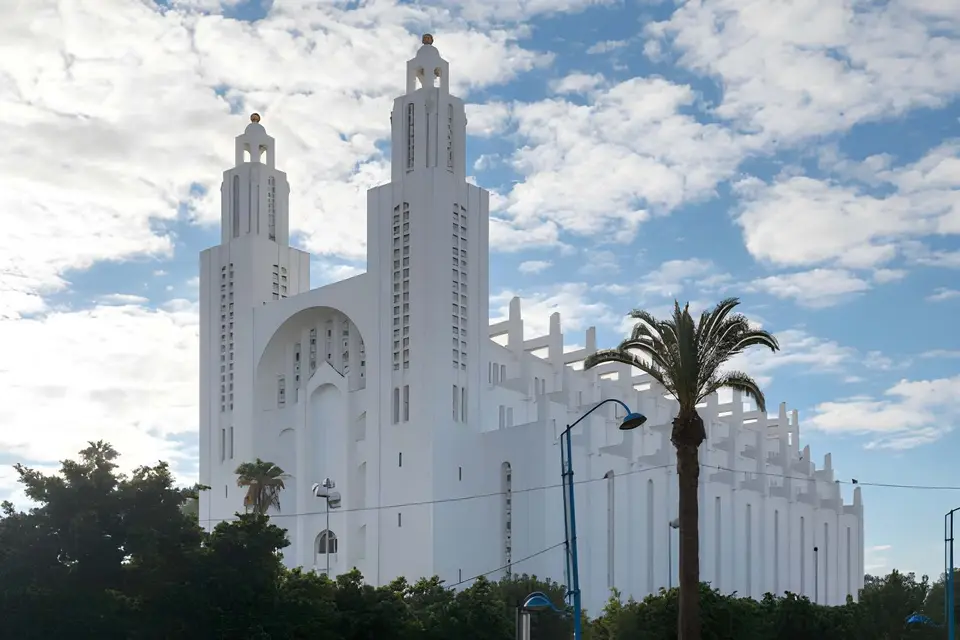 A white cathedral with twin spires and a palm tree under a cloudy sky