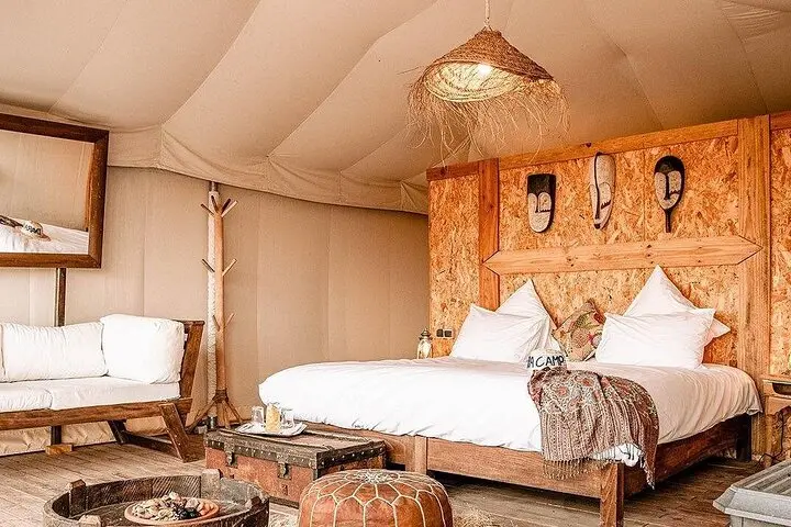 Inside a camp tent: a double bed, a carved wooden headboard and a woven lamp