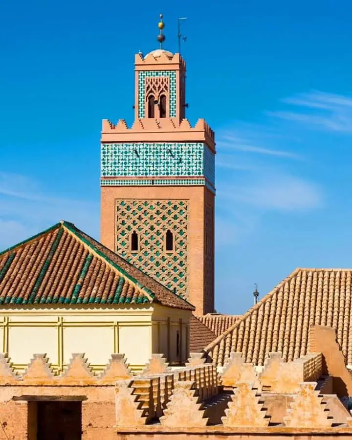 A tiled minaret above green-tiled roofs against a blue sky