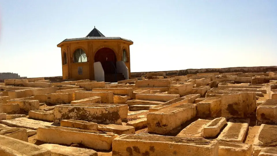 Excavated stone ruins beside a small domed pavilion under a clear sky