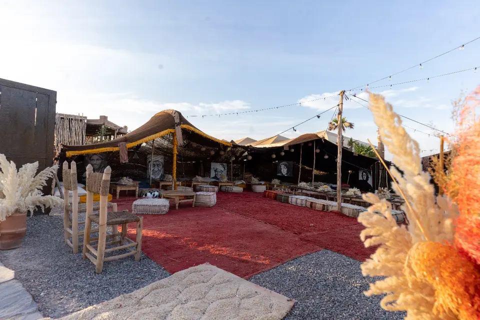 A camp lounge under an open tent, with rugs, low seats and lanterns